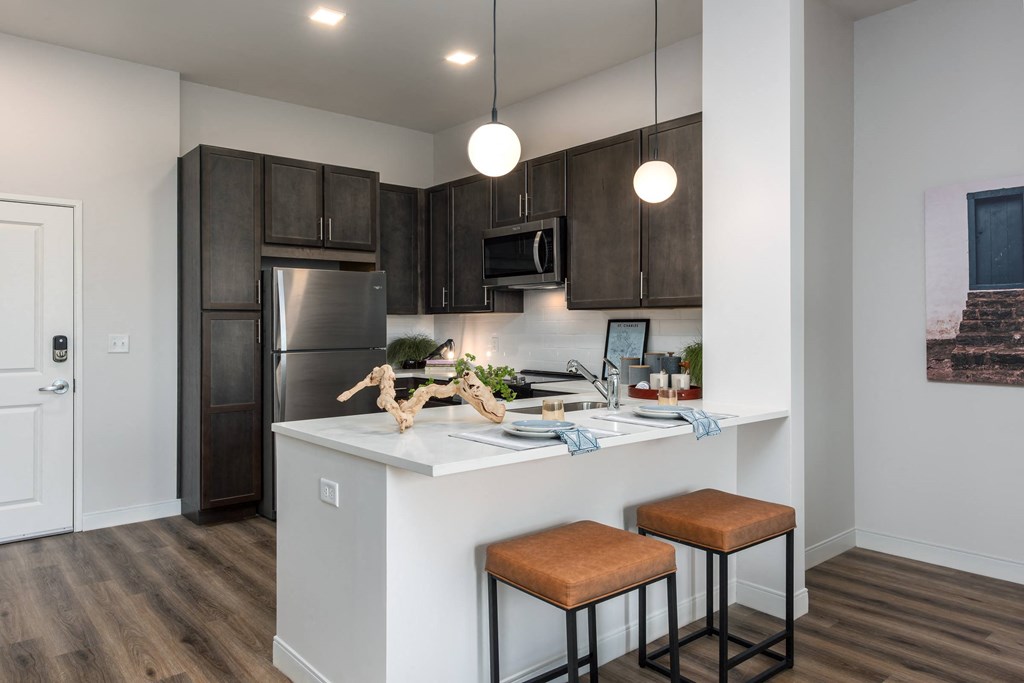 Modern kitchen with designer lighting, dark cabinetry, stainless steel appliances and counter with seating  at Chapter at the Streets of St Charles, Saint Charles, 63303