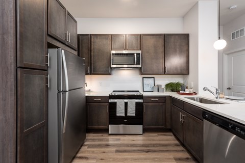 Modern kitchen with designer lighting, dark cabinetry and stainless steel appliances  at Chapter at the Streets of St Charles, Saint Charles, MO