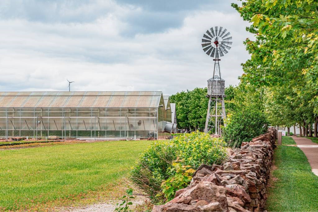 A windmill stands next to a green field with a stone wall in the foreground.