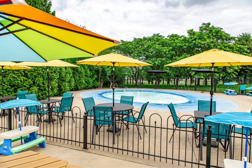 A pool area with a table and chairs under umbrellas.