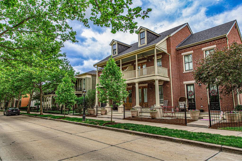 A red brick house with a balcony and a tree in front.