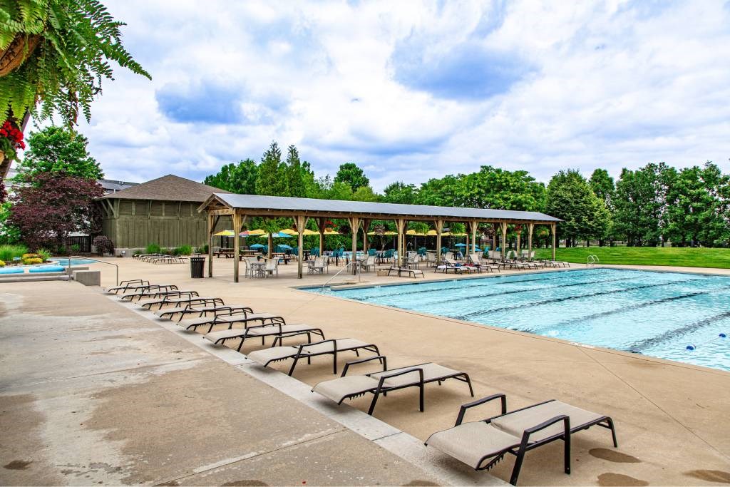 A pool with sun loungers and a pavilion in the background.