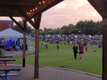 A large gathering of people are sitting on the grass under a tent.