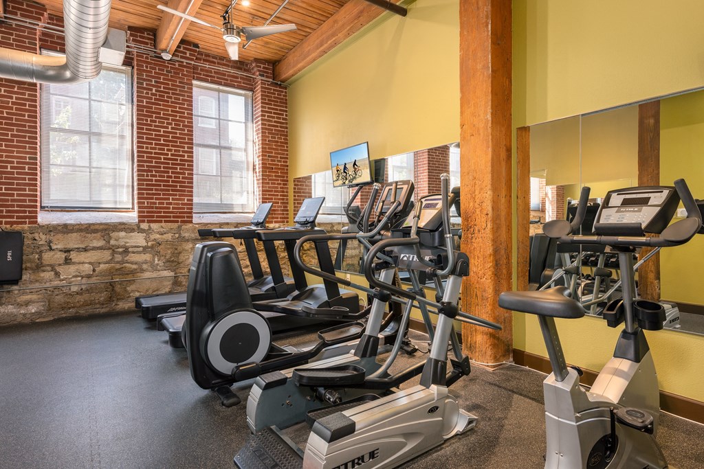 a gym with cardio equipment and weights in a building with brick walls at Lofts at Lafayette Square Apartments, Saint Louis, MO