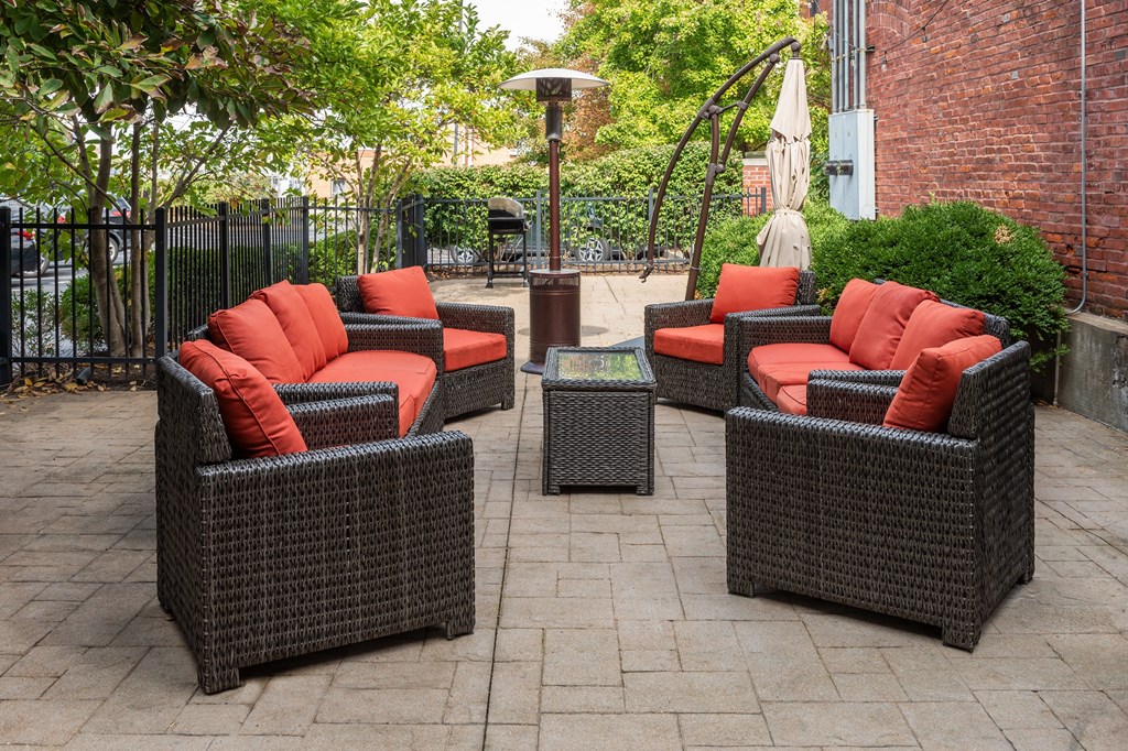 a patio with wicker furniture and orange pillows on it at Lofts at Lafayette Square Apartments, Saint Louis, MO