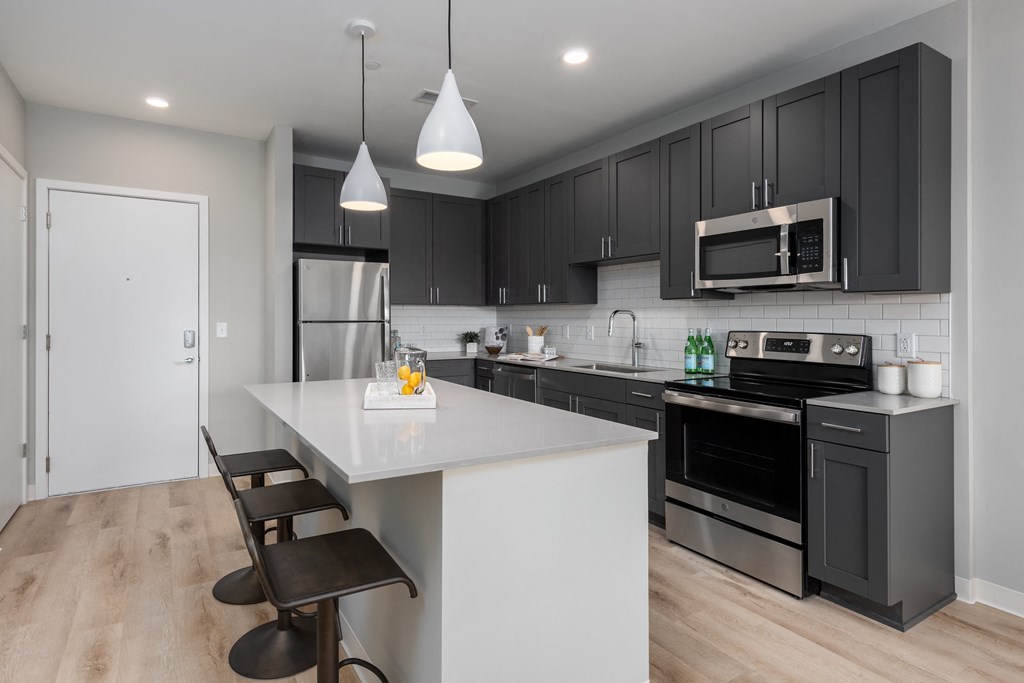 an open kitchen with a large white island and black cabinets at The Edwin on Grand Apartments, Missouri