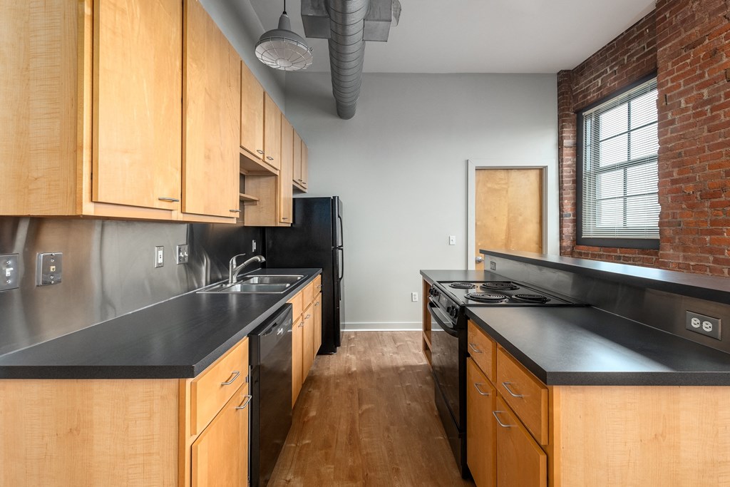 a kitchen with wooden cabinets and black counter tops and a brick wall at Lofts at Lafayette Square Apartments, Saint Louis, MO, 63104