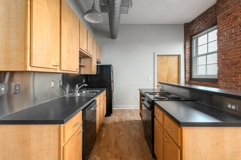 a kitchen with wooden cabinets and black counter tops and a brick wall