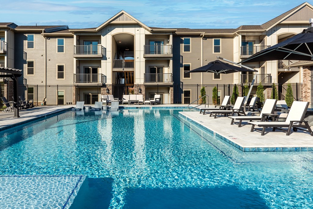 a swimming pool with chairs and umbrellas in front of an apartment building at The Station St. Peters, St. Peters, 63376