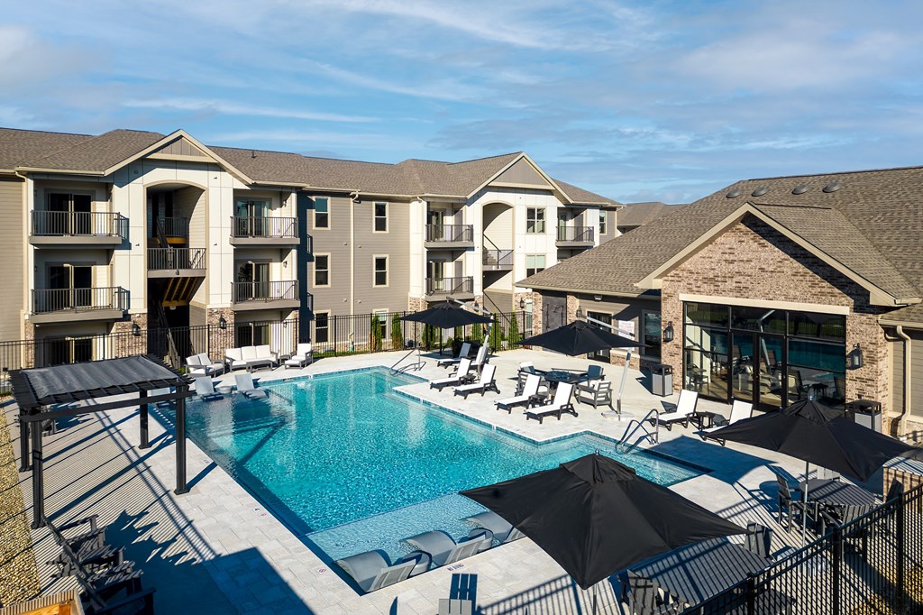 a swimming pool with chairs and umbrellas in front of a building at The Station St. Peters, St. Peters, MO