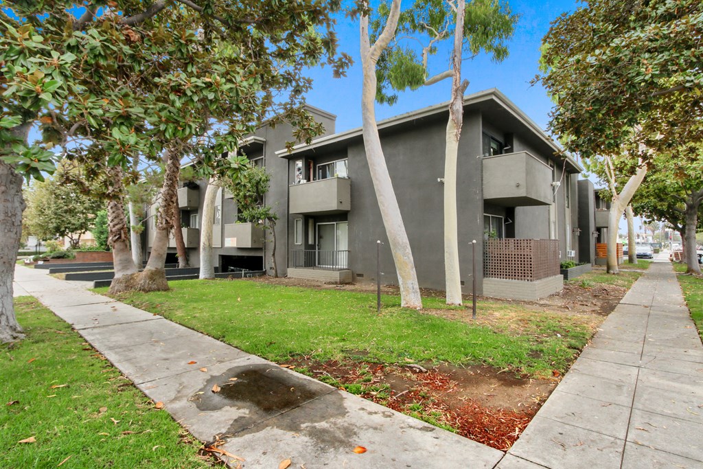 a grey apartment building with trees and a sidewalk