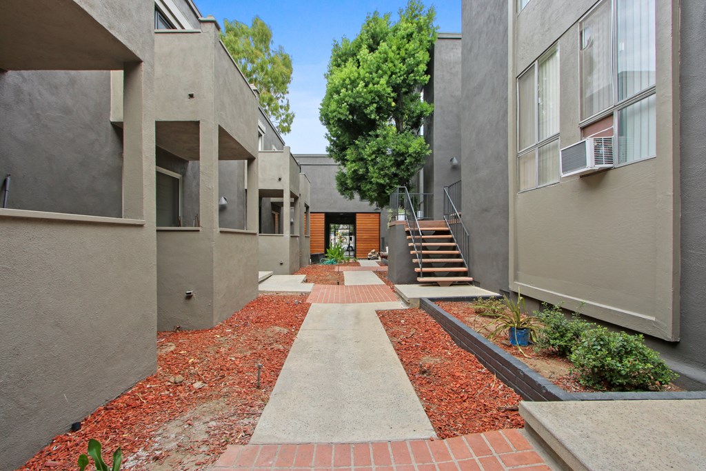 a walkway between two buildings with stairs and a tree