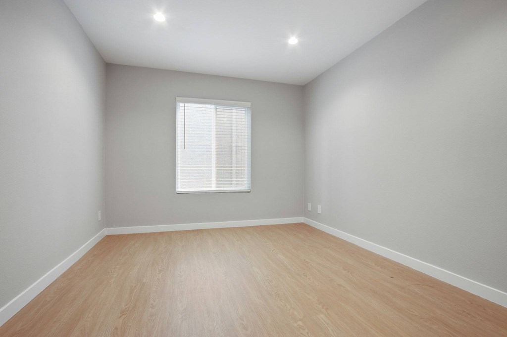 A room with wooden flooring and a window with blinds.