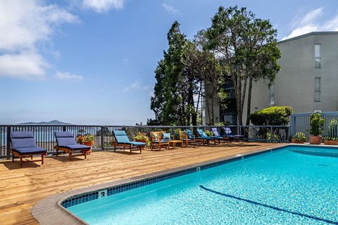A pool with a wooden deck and chairs in front of a building.