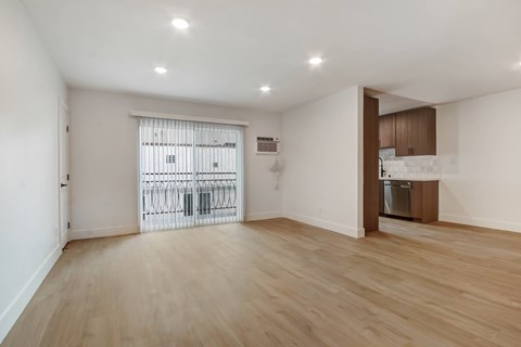 A spacious room with wooden flooring and a sliding door leading to a balcony.