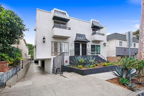 A white two-story house with a black gate and plants in front.