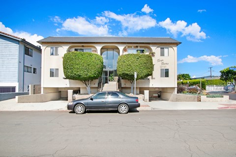 A car is parked in front of a two-story building with green plants on the front.