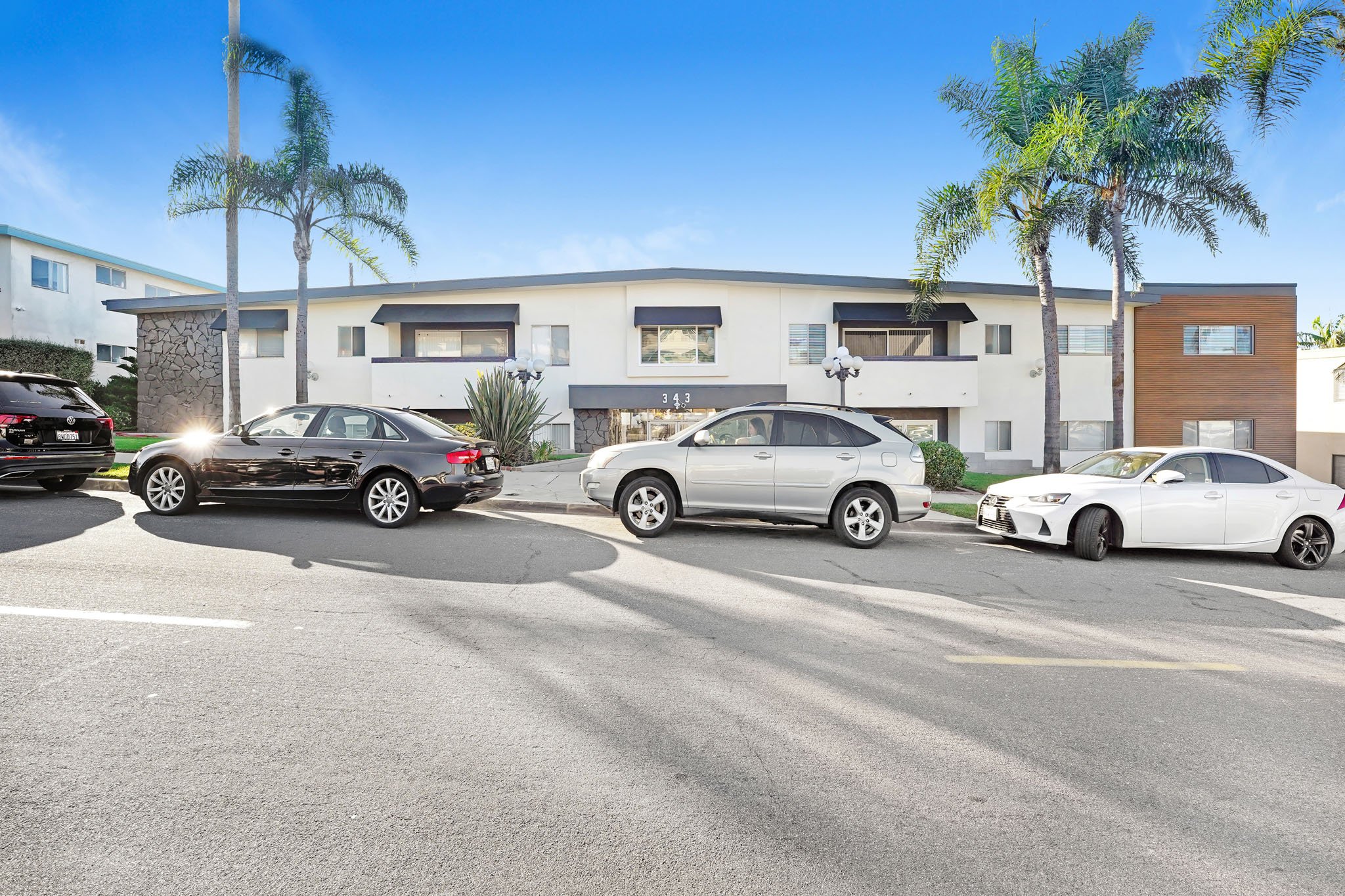 A black car is parked in a parking lot in front of a white building.