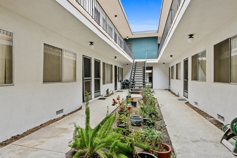 A long white building with a balcony and plants on the ground.