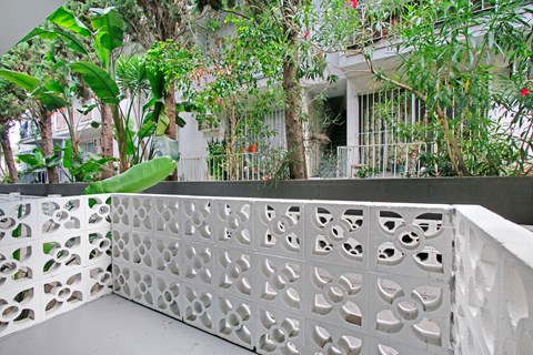 A white lattice fence with circular cutouts separates a patio from a lush green garden.
