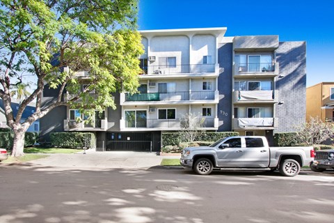 A silver truck is parked in front of a modern apartment building.