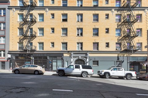 A tan car is parked in front of a building with a fire escape.