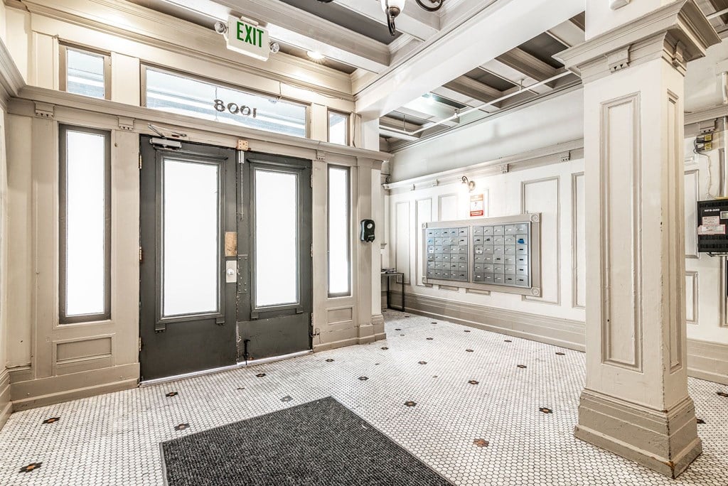 A hallway with a black and white checkered floor and a green exit sign above the door.