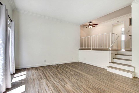 an empty living room with stairs and a ceiling fan