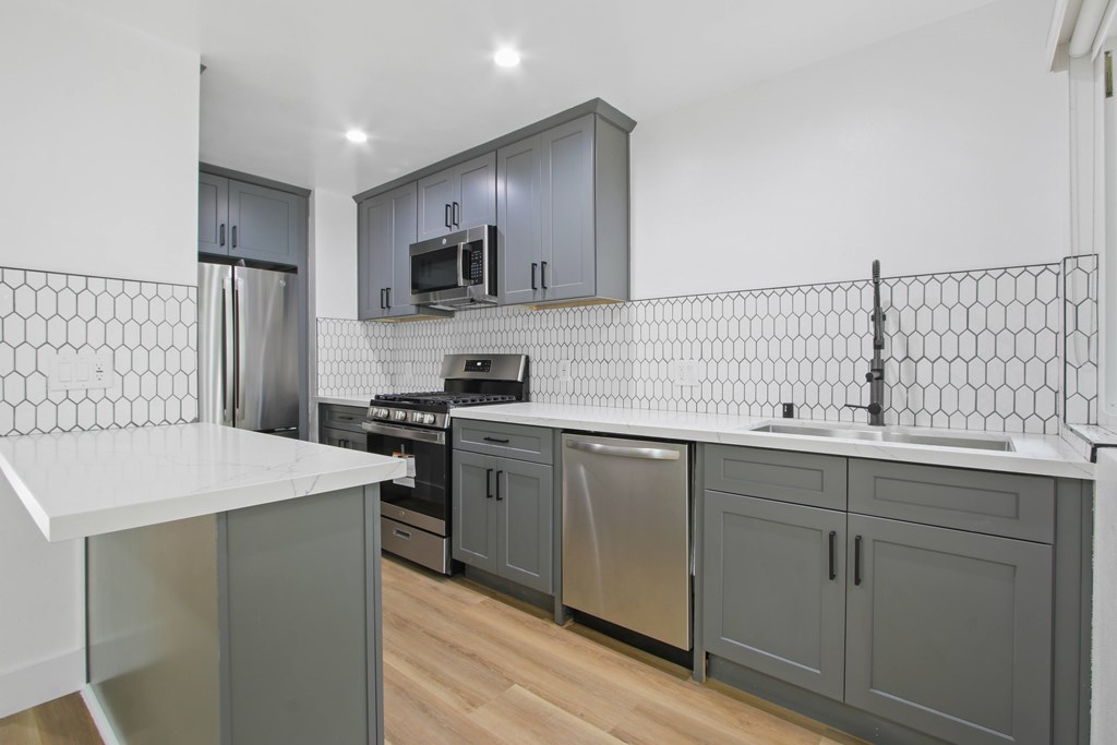 A kitchen with a white counter top and grey cabinets.