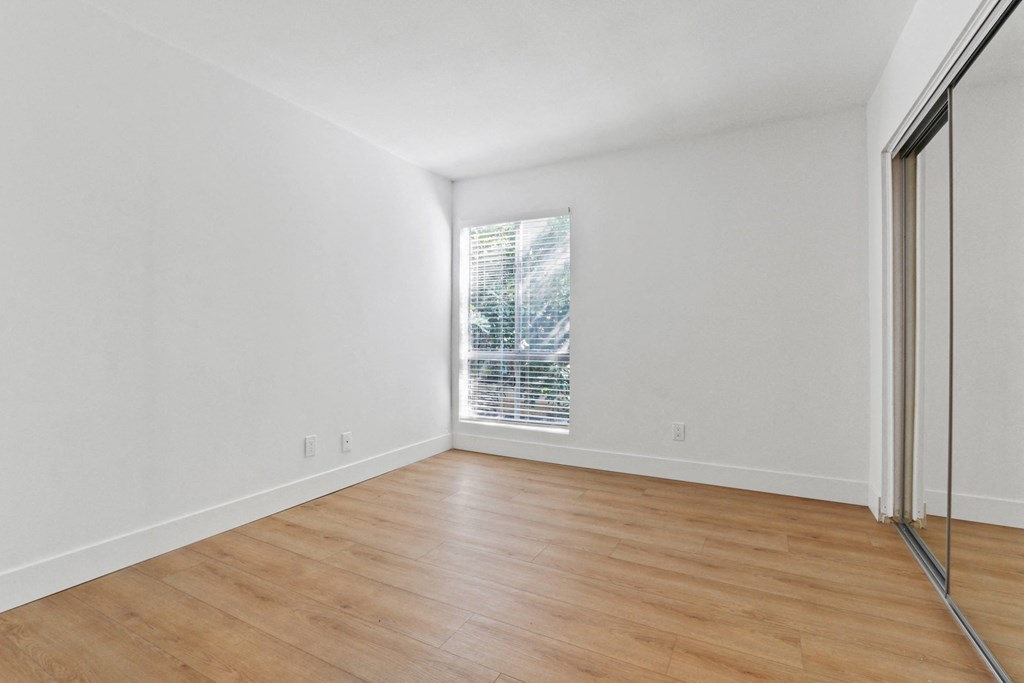 a living room with white walls and wood floors and a window