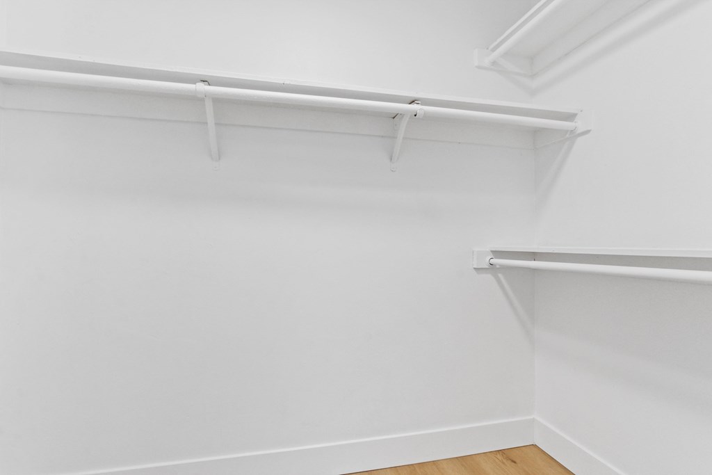 an empty closet with white walls and white rails and a wooden floor