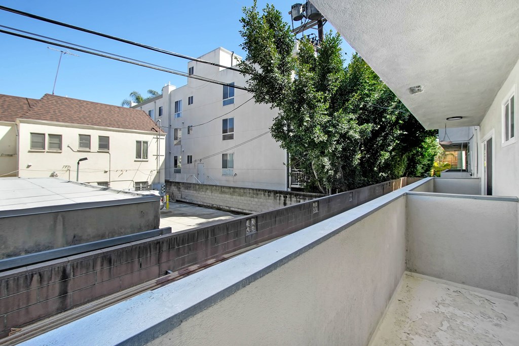 A balcony with a white wall and a tree in the background.