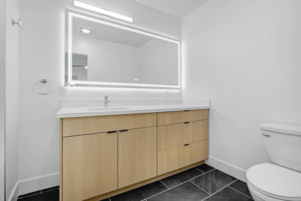 A bathroom with a white toilet, a sink with a mirror above it and a cabinet below it.
