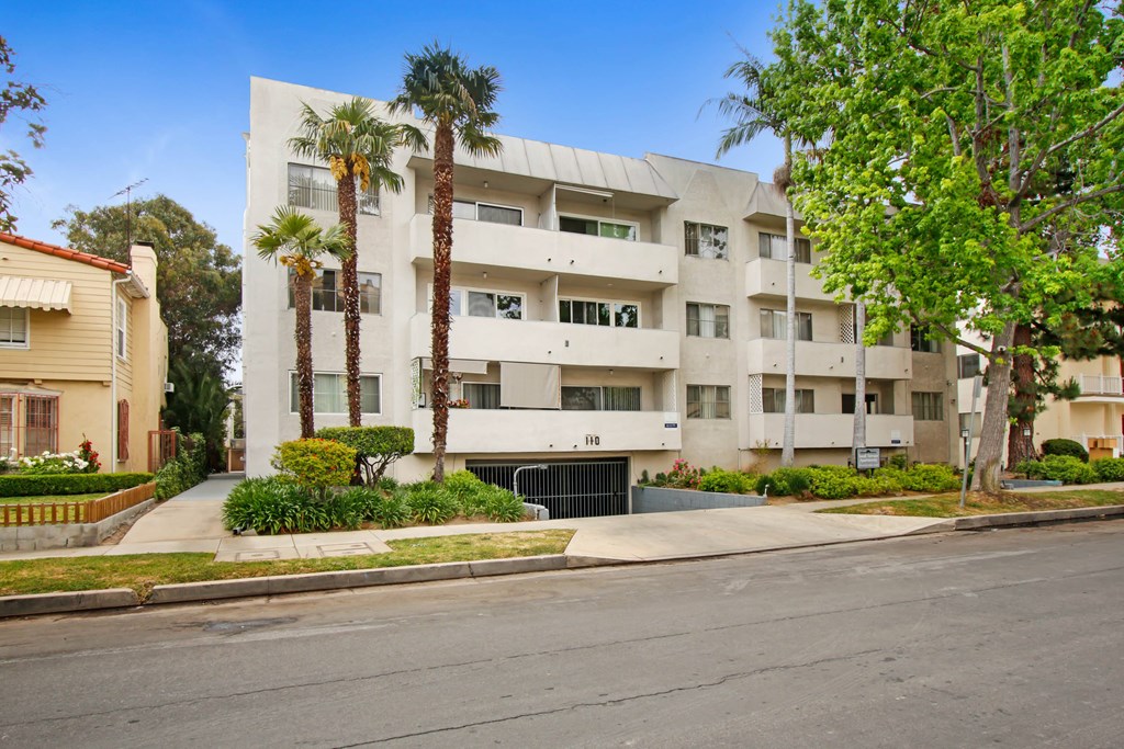 A modern white apartment building with palm trees in front.