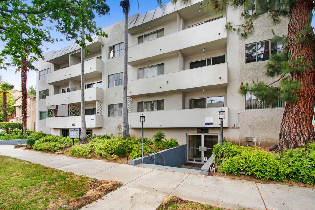 an apartment building with a sidewalk and trees in front of it