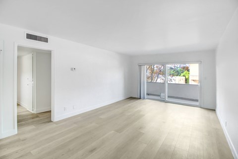 A room with a white wall and a window with a view of trees and a building outside.