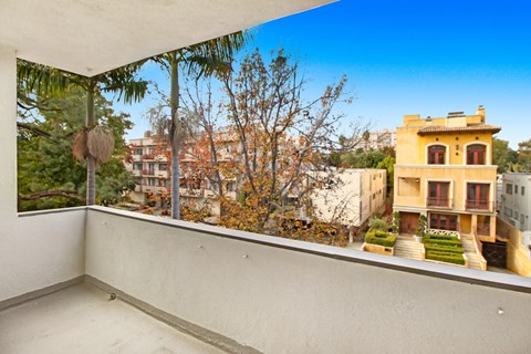 A balcony with a view of a yellow building and trees.