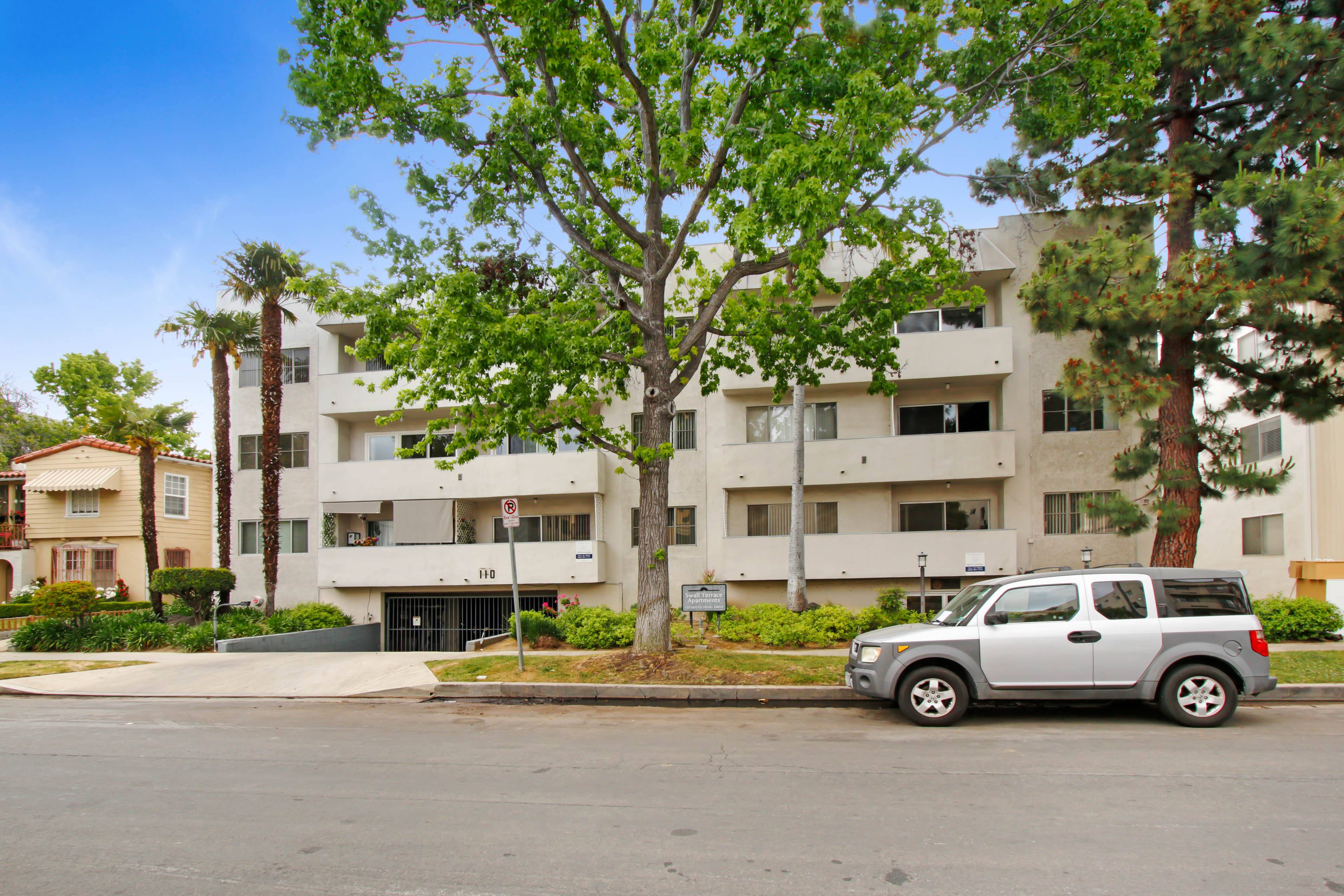 A silver car is parked in front of a white apartment building.