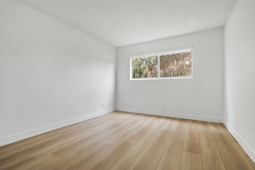 A room with wooden flooring and a window showing a view of trees.