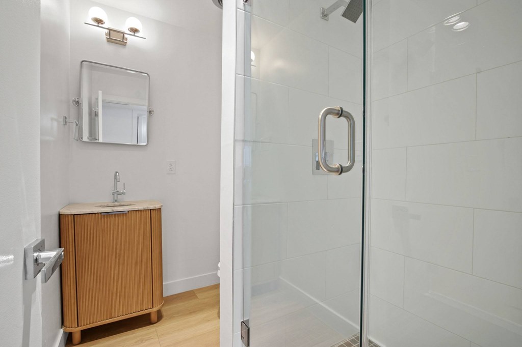A bathroom with a glass shower door and a wooden cabinet.