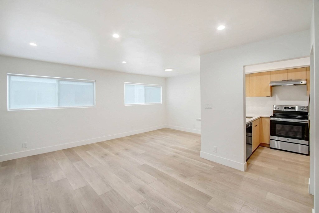 the living room and kitchen of a new home with wood flooring and appliances