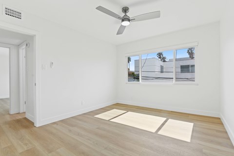 A room with a ceiling fan and a window overlooking a building.