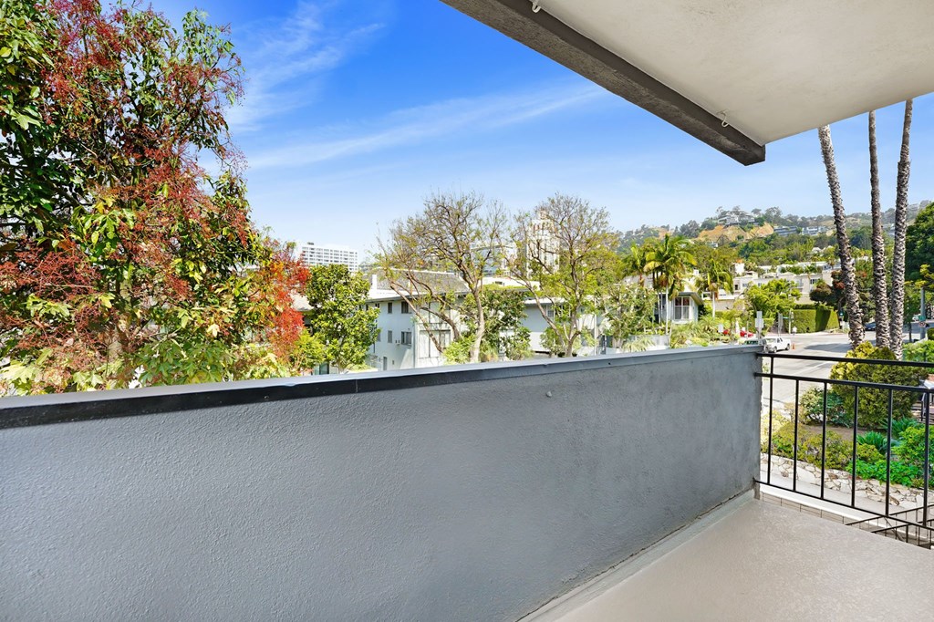 A balcony with a grey wall and a view of trees and buildings.