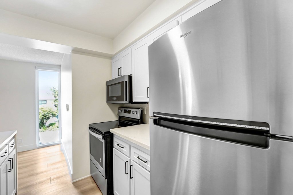 A stainless steel refrigerator stands in a kitchen with white cabinets and black appliances.