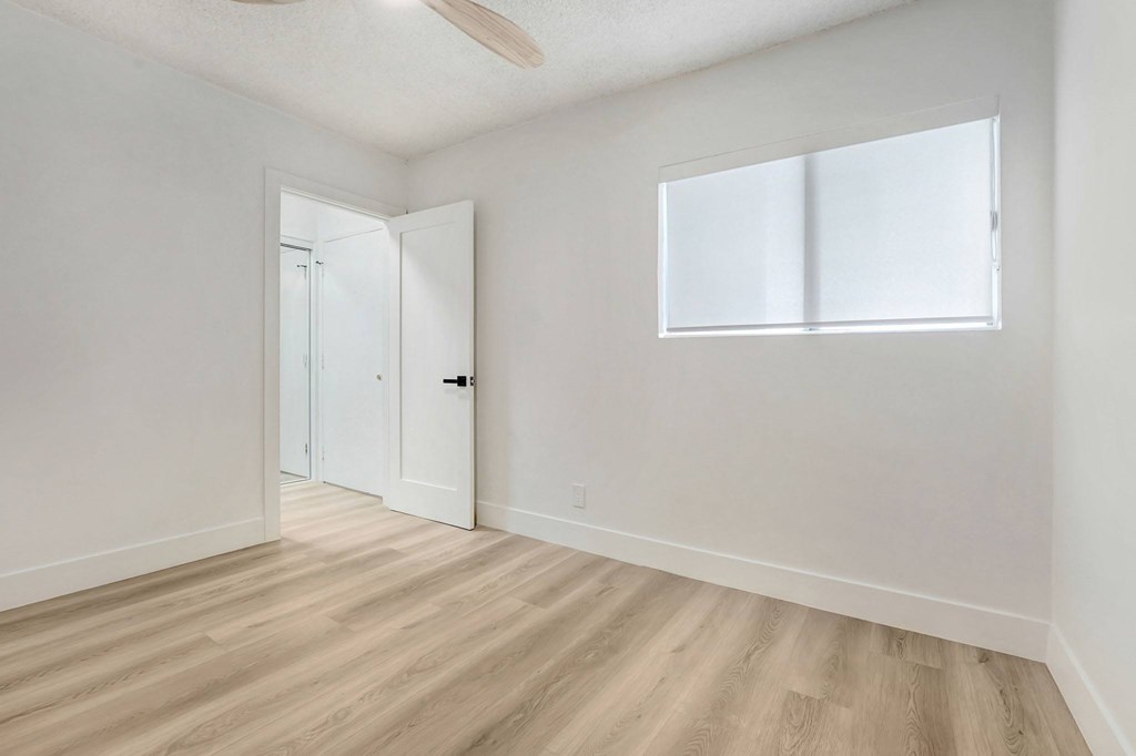 A room with a white door and a window with white blinds.