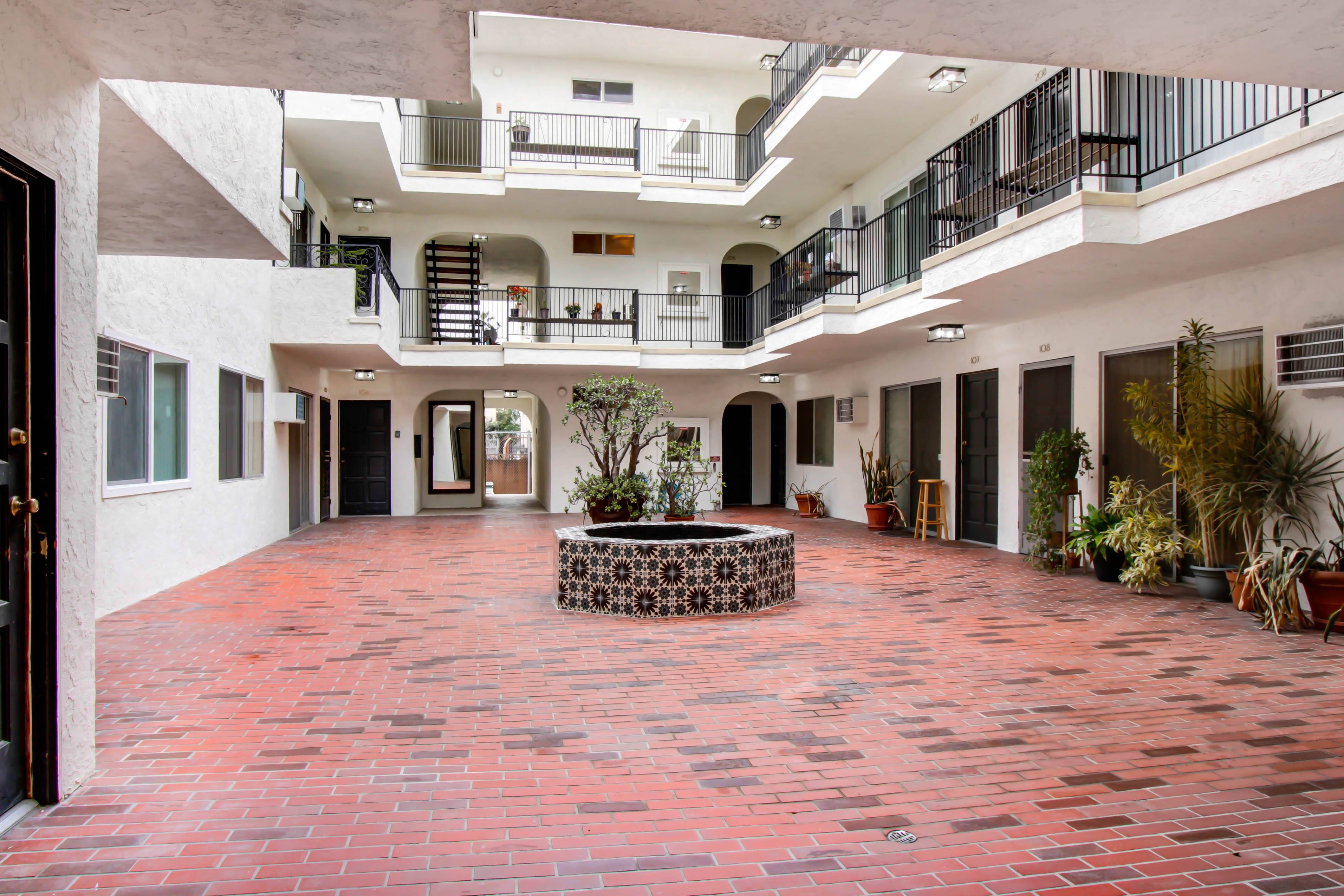 A courtyard with a red tile floor and a fountain in the middle.