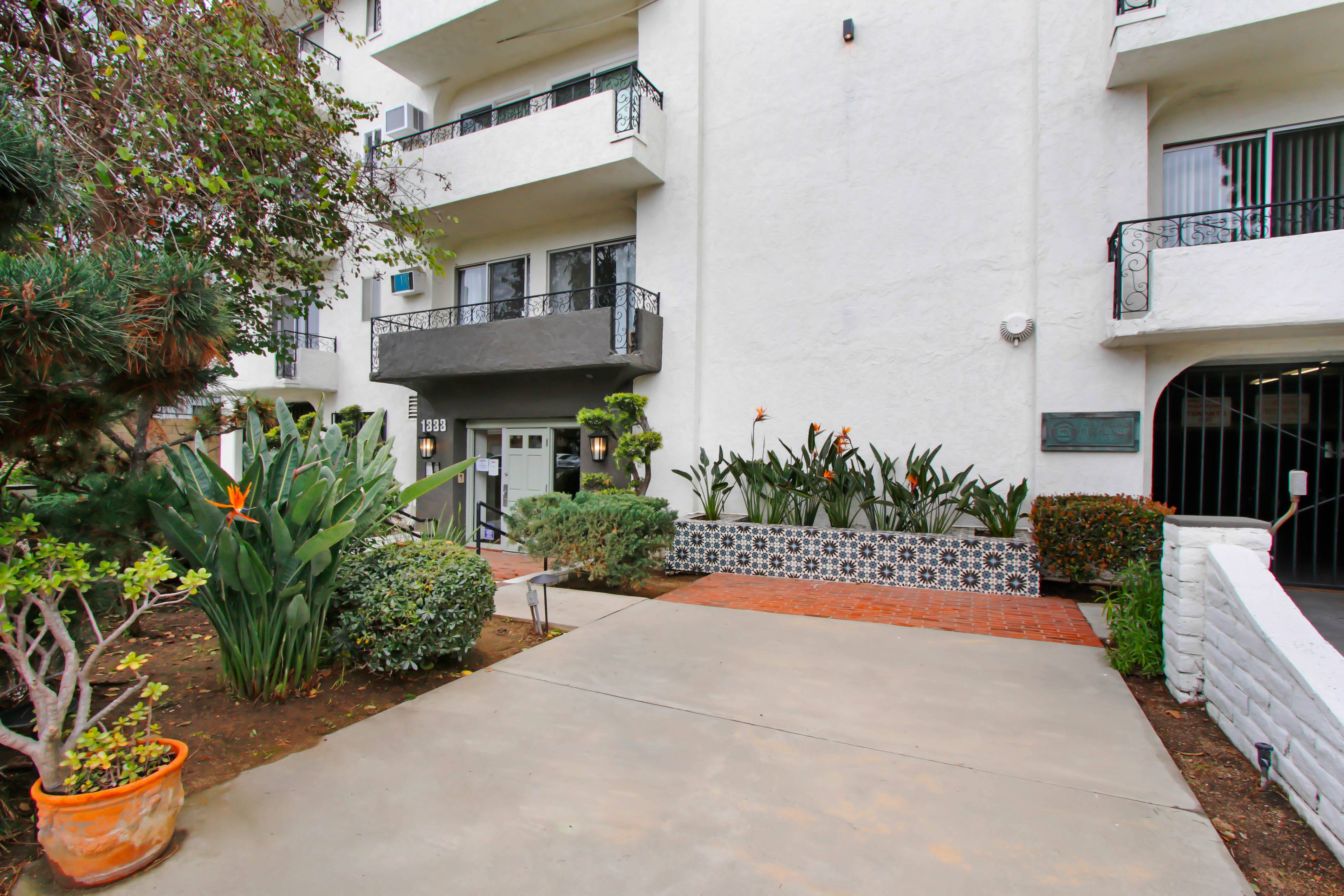 A white building with a balcony and a small garden in front.