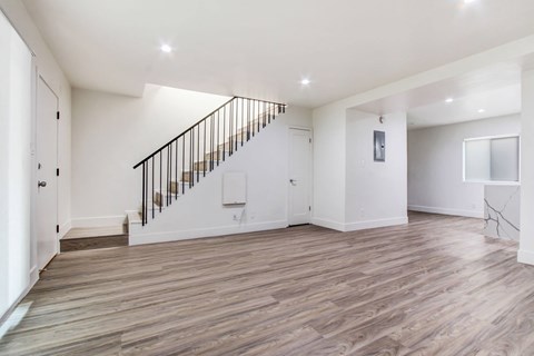 A spacious room with wooden flooring and a staircase with a metal railing.