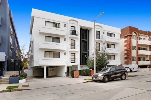 A modern white apartment building with a black car parked in front.