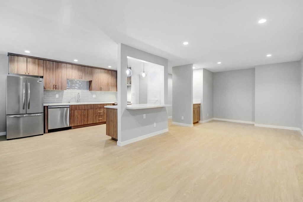 an empty living room with a kitchen with stainless steel appliances